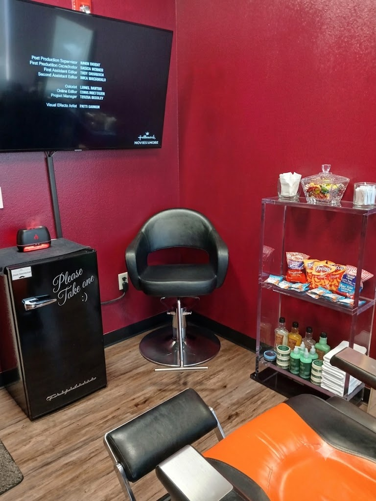 Comfortable client lounge with a wall-mounted TV, a complimentary snack and drink shelf, and a mini fridge